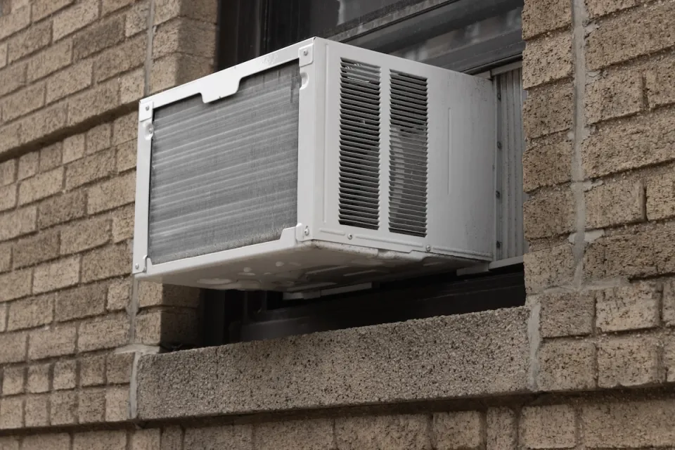 Close-up of white air conditioning window unit in window of brown brick building.